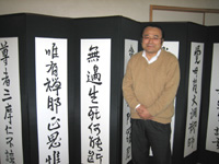 スタッフの休憩ルームに置いてある直筆の書道の前に立つ矢山先生。